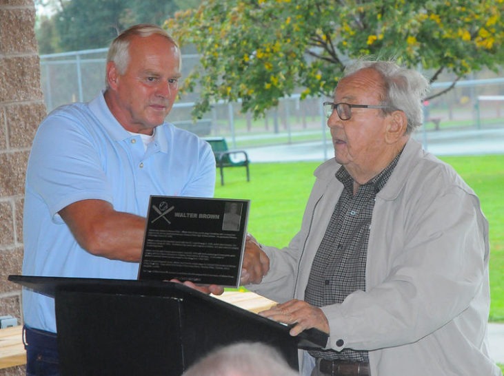 Town of Ellery supervisor Arden Johnson, right, presents a plaque to Tom Brown, son of the late Walt Brown, on Saturday. The town is dedicating a Little League field in the name of Walt, a Bemus Point native and former major league pitcher. 