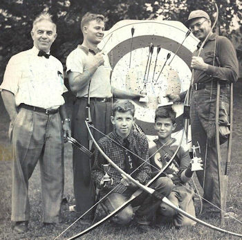 Louis Collins, a CSHOF inductee is standing with 4 boys and men, who are holding bows, by an archery target.,