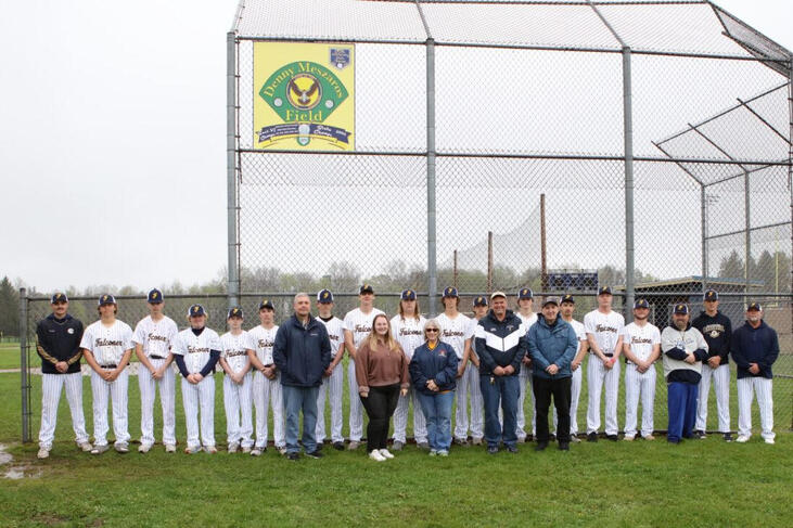 Family members, Falconer Central School administration and faculty, and the Golden Falcons’ varsity baseball team stand below the new Denny Meszaros Field sign.